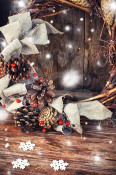 Woven from twigs and decorated with pine cones Christmas wreath on snowy wooden background.