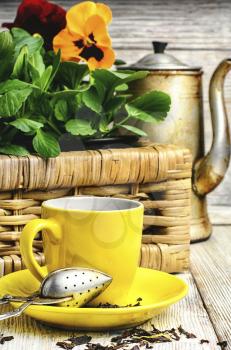 Yellow porcelain cup with tea and basket of decorative Pansy