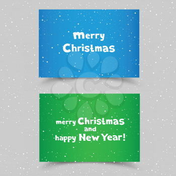 The colored blue and green pieces of paper with the white message of Christmas greetings on gray snow background