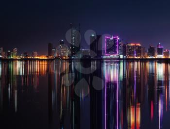 Night modern city skyline with shining neon lights and reflection in the water. Manama, the Capital of Bahrain, Middle East