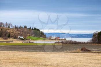 Spring rural Norwegian landscape with wooden houses and dry field