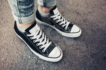 Black and white new sneakers, teenager feet stand on dirty urban pavement. Closeup photo with selective focus