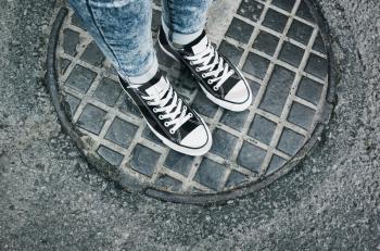 Teenager feet in sneakers. Gumshoes standing an urban manhole cover. Closeup photo with selective focus and vintage blue tonal correction filter, old style 