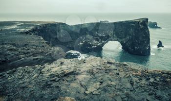 Natural rocky arch. Scenic landscape of Dyrholaey Nature Reserve, south coast of Iceland, Europe. Blue toned vintage stylized photo