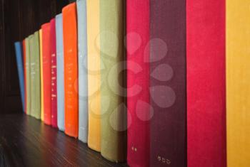 Old books in colorful covers stand on wooden shelf