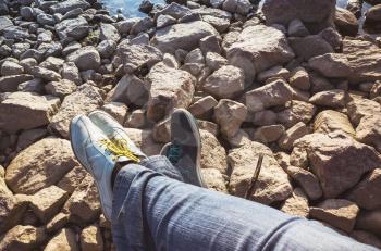 Male and female feet in sporty shoes lay on coastal rough stones. Family travel lifestyle background