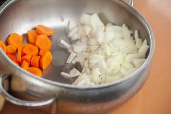 Sliced orange carrots and white onions are in steel bowl on a kitchen table