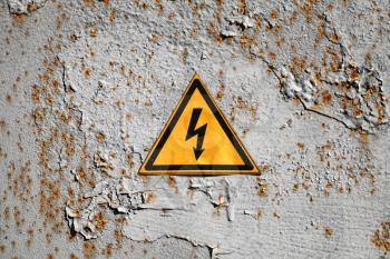Yellow high voltage triangle warning sign on rusty gray metal wall
