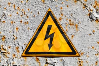 Yellow high voltage triangle warning sign on rusty gray metal wall, close-up photo