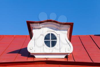 Vintage attic window on red roof slope in decorative white wooden frame