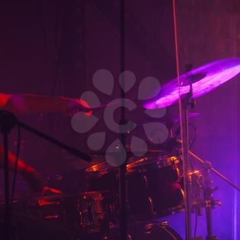 Live rock music photo background, drummer plays on rock drum set  with cymbals in purple stage lights. Close-up photo, soft selective focu