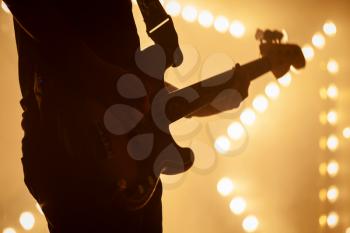 Electric bass guitar player in stage strobe lights, close-up silhouette photo with soft selective focus
