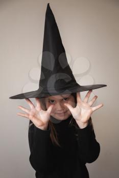Little blond European girl in black witch costume posing over white wall, close-up studio portrait