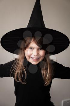 Little blond girl in black witch costume posing over gray wall, close-up studio portrait
