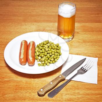 Daily food theme. Sausages with mustard, green peas and glass of beer on wooden table