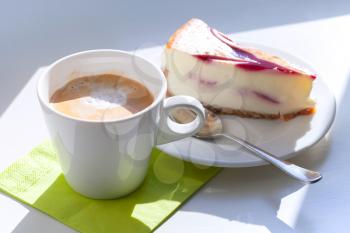 Cup of cappuccino coffee and cheesecake piece on white table