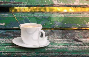 Cup of hot coffee with cream is on old wooden bench in autumn park.  Selective focus with shallow DOF