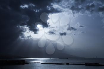 Sunlight goes through dark stormy clouds. Bay of Izmir, Turkey. Blue toned stylized photo