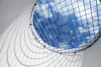 Abstract white interior fragment. Blue cloudy sky behind the round window with metal grid