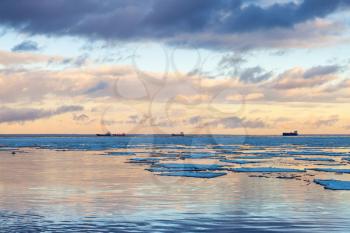 Winter coastal landscape with big ice fragments, and cargo ships on the horizon. Gulf of Finland, Russia