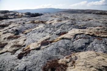 Norwegian mountain landscape, dark gray flat rocks and moss under blue sky