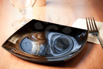 An empty black plate with fork and glass on the wooden table