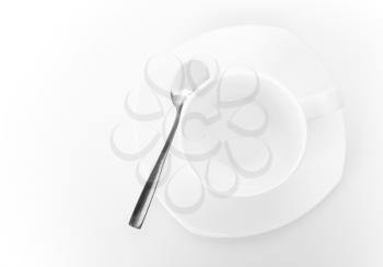 White ceramic cup on saucer with metal spoon above white background. Top view