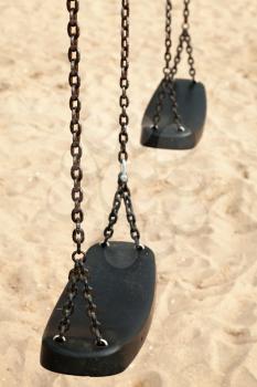 Empty swings made of black plastic and steel chains on a sandy beach, closeup photo with selective focus and shallow DOF