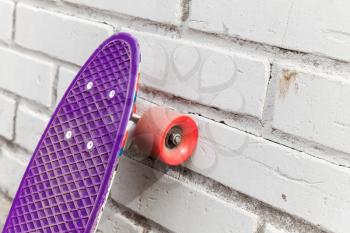 Modern purple skateboard stands near white brick wall, close-up fragment