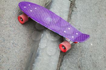 Modern skateboard stands on the curb of asphalt road