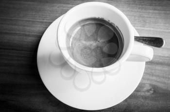 White cup of freshly brewed espresso coffee on saucer with spoon. Black and white photo with selective focus
