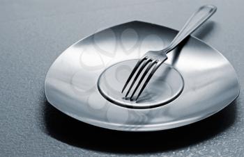 Empty steel plate with fork on the table. Monochrome photo with shallow depth of field