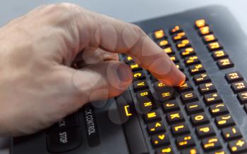 Finger pressing Y key on illuminated industrial keyboard. Selective focus