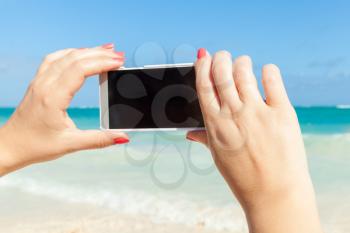 Woman using smart phone for taking outdoor photo on a beach in Dominican republic