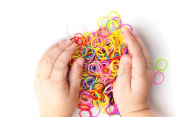 Little child hands and pile of small colorful rubber bands for making rainbow loom bracelets on white background