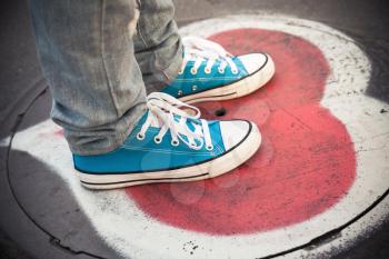 Blue sneakers, teenager feet standing on urban sewer manhole with heart sigh