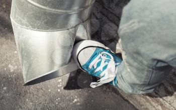 Teenager in blue sneakers kicks drainpipe, aggression concept. Vintage tonal correction, old style filter effect