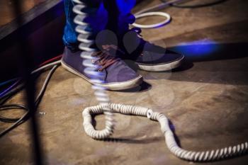 Rock and roll theme. Feet of bass guitar player on a stage with white wire. Selective focus