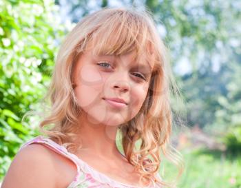 Portrait of a slightly smiling little blond beautiful Russian girl above nature outdoor background
