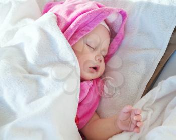 Baby girl sleeps under pink and white cotton towels with a pacifier nearby