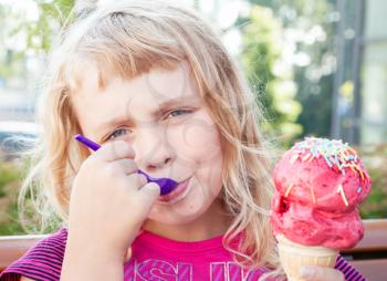 Little girl eats big fruit ice-cream in the park