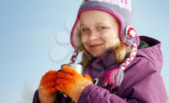 Smiling little blond girl in cold season wears winter outwear with metal thermos cup of hot tea