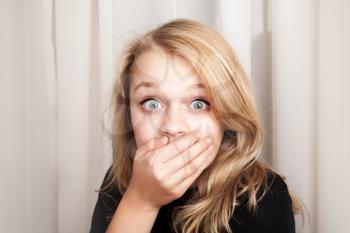 Beautiful blond Caucasian surprised girl opened her eyes wide and covers her mouth with her hands, closeup studio portrait