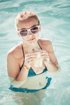 Little blond girl drinks cocktail in swimming pool, vintage toned photo filter effect