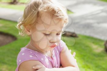 Outdoor closeup portrait, funny Caucasian blond baby girl resentfully pouts