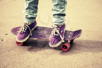 Teenager feet in jeans and gumshoes on a skateboard, photo with warm retro tonal correction, 
old style