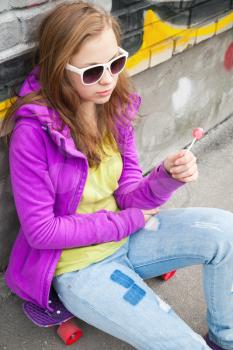 Blond teenager girl with a lollipop, vertical urban outdoor portrait