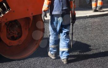 Urban road under construction, asphalting in progress, worker with a shovel near orange  roller