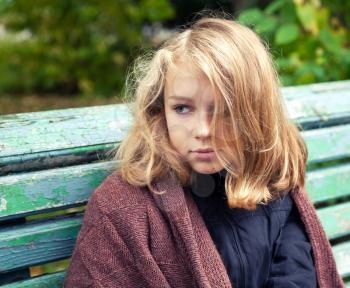 Beautiful Caucasian blond teenage girl in brown woolen plaid sitting on old green bench in autumn park
