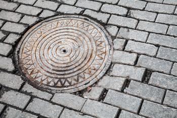 Round steel sewer manhole on the cobblestone road